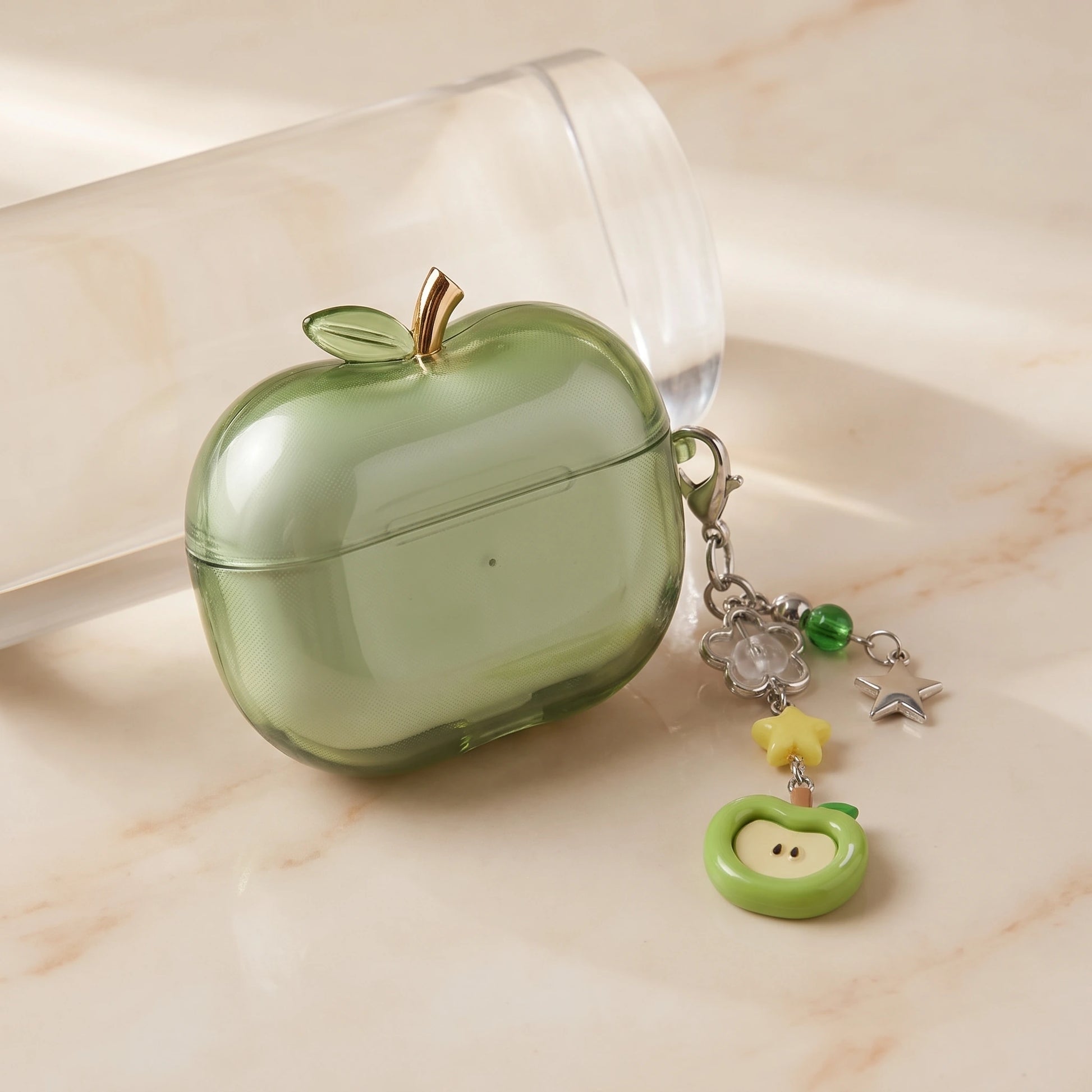 Green translucent apple-shaped AirPods case with charm chain on cream marble