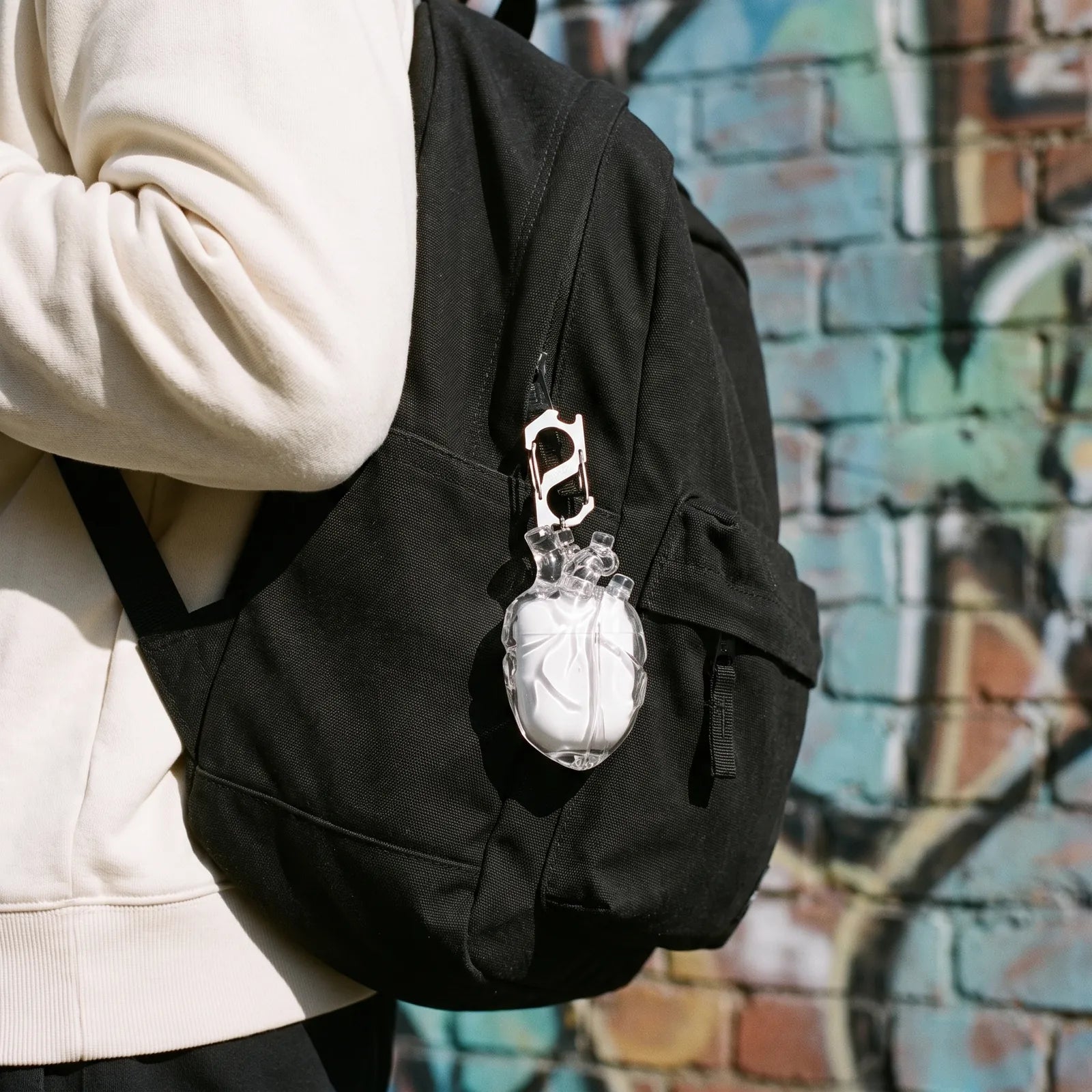 Clear heart AirPods case clipped to a black backpack strap
